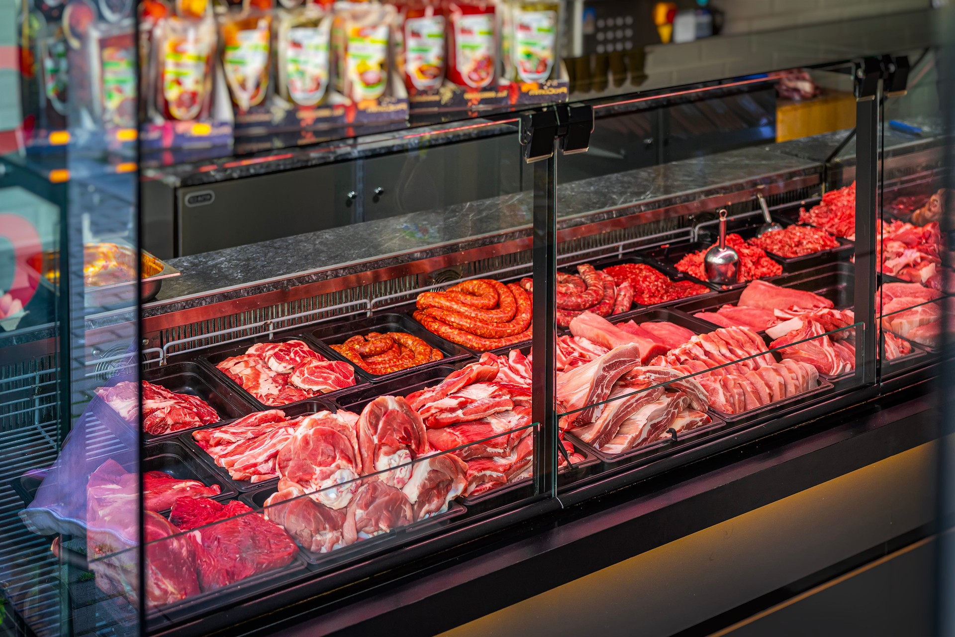 Meat counter. Butcher shop fridge counter with assortment of raw meat.. Glass display case in butcher shop filled with fresh meat products. Various cuts of beef, pork, sausages are arranged for buyers
